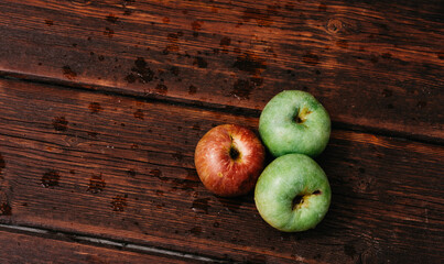 Fresh apples, autumn harvest. Three apples - two green and one red-lie on a wooden table. Fresh apples on a wood textured brown background, mahogany material.
