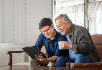 Happy senior asian father and adult son using tablet smartphone in living room