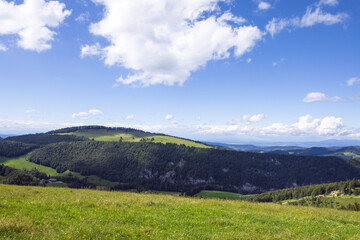 Fresh green meadow on slopes of Jura mountains and valley, swiss idyll landscape, summer day. Naturpark Thal, Switzerland.