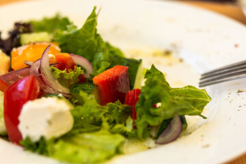 Greek salad on a white plate in a summer cafe. Vegetarian dish. Olives, purple onions and feta cheese. Light snack in a cafe. Summer menu. Natural light.