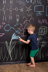 three-year-old boy draws with multi-colored chalk on a large blackboard. black wall with children's drawings and formulas. vertical photography.