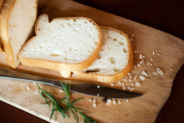 Sliced gluten-free white bread, salt and pepper, herbs on a wooden background.