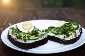 two sandwiches with microgreens, cucumber and quail eggs on a white plate. wooden background. a kind of sunshine. Healthy diet. Delivery option. young sprouts of radish and red cabbage