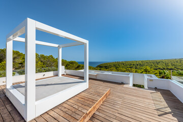 white square structure on the roof of a house with wooden floors overlooking a pine forest and the sea, clear blue sky