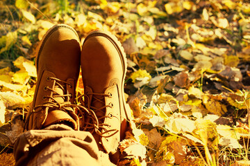 Girl's legs in brown leather shoes on autumn yellow foliage, close-up. Walk in the autumn forest on a sunny fall day