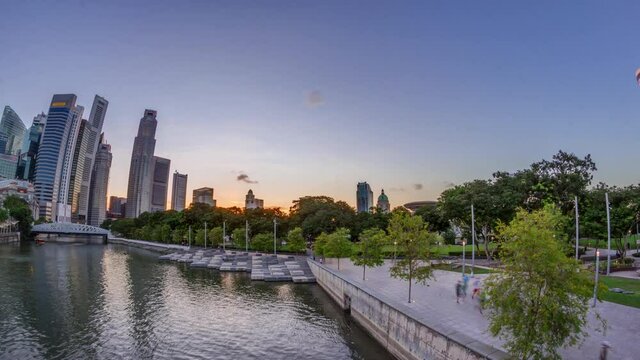 Sunset over Singapore skyscrapers skyline with white Anderson Bridge and a few towers of financial district near esplanade park timelapse. Some green foliage on both sides.