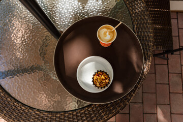 Glass of cappuccino and cake on a tray. Morning Breakfast in the summer cafe. Top view of a tray with food on the table. Sweet snack. Cake with nuts. Beautiful brown color of the image. Warm shade.
