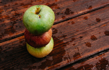 Pyramid of three apples. Fresh apples, autumn harvest. Three apples - green, yellow, and red-lie on a wooden table. Fresh apples on a wood textured brown background, mahogany material.