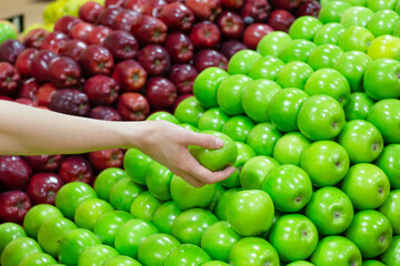 Closeup of a person's hand choosing a green apple from a pile at the grocery food market stall.