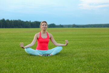 young woman doing yoga exercises on a large meadow of lawn grass