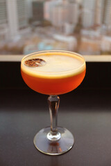 Vivid orange cocktail drink on the rooftop terrace table against blurry urban aerial view