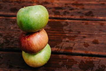 Pyramid of three apples. Fresh apples, autumn harvest. Three apples - green, yellow, and red-lie on a wooden table. Fresh apples on a wood textured brown background, mahogany material.
