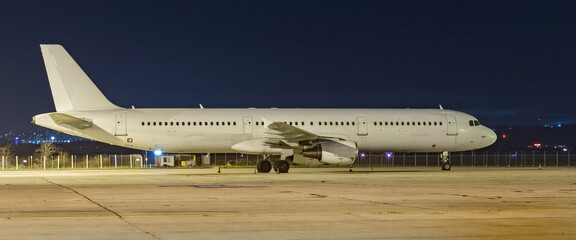 Side view of white airplane on dark night sky background. Jet commercial aircraft on airport apron, low night light. Modern technology in fast transportation, private business travel, charter flight.