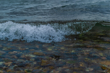 bright dark green waves of lake baikal, pebbles, stones in water, coast summer