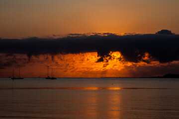 Naklejka premium Beautiful sunrise on beach with boats in distance with clodscape