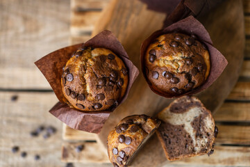 Soft and moist chocolate banana muffins with dark chocolate drops in wooden box, rustic table. Homemade baked twisted cupcakes. Natural light, selective focus, copy space