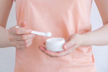 A jar of face cream in the hand of Caucasian woman. White background.