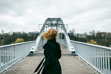 Lonely woman in black coat on footbridge in autumn.