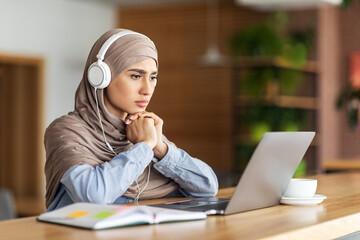 Girl in headscarf having online lesson on laptop at cafe