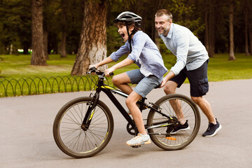 Boy learning to ride bicycle with his supportive dad
