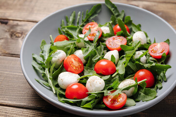 Diet and healthy salad with arugula, cherry tomatoes, mozzarella cheese on wooden background