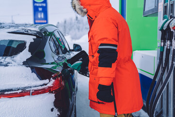 Cropped image of male traveler in warm winter coat refilling car tank on gas station during journey,rear view of man driver checking petrol barrel on transportation