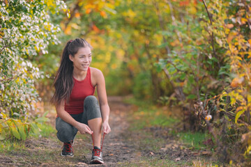 Autumn outdoor exercise lifestyle. Asian runner woman tying running shoes ready to run for fitness cardio workout in forest nature.