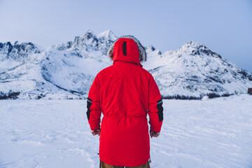 Back view of male in red winter coat looking at cold white mountains peaks in snow satisfied with scandinavian vacation, man explore wanderlust destination in Finland