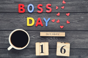 Colorful inscription Boss Day with cup of coffee and calendar on black wooden background