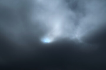 Imagen del Sol que sale a través de una fina capa de nubes en medio de un cielo totalmente nublado. Color, gris, blanco y azul