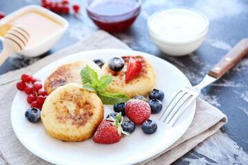 Tasty cheese pancakes with berries, bowls with honey, jam and cream on grey background