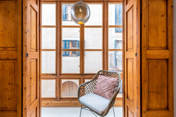 Mallorcan style wooden window with views to the outside, in the middle a chair and a designer lamp