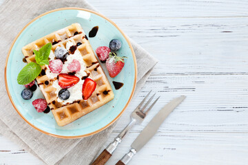 Tasty waffles with fresh berries and whipped cream on white wooden background