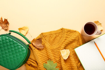 Woolen sweater with green bag, cup of tea and autumn leafs on beige background