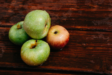 Fresh autumn Apple harvest on the kitchen countertop. Four fresh apples lie on a wooden table. A textured mahogany wood background and fruit lie on it.