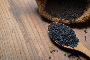 Heap of black Sesame close-up shot on a wooden spoon and in a sack, wooden background
