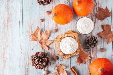 Pumpkin pie smoothie on worn wooden table with cedar cones and dry leaves. Autumn still life with pumpkin smoothie decorated with whipped cream closeup