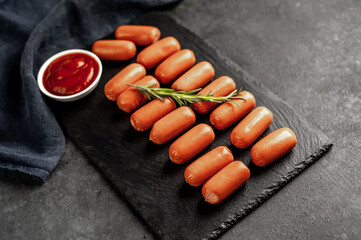 raw mini sausages with spices and ketchup on a slate board on a stone background