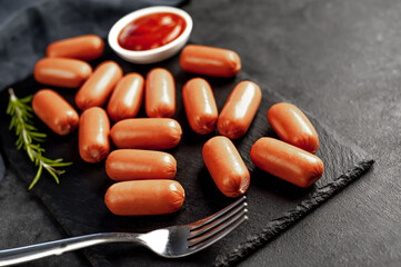 raw mini sausages with spices and ketchup on a slate board on a stone background