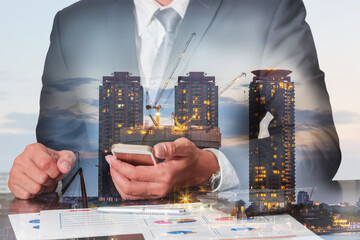 Double exposure of businessman working with smartphone construction crane and building in the...