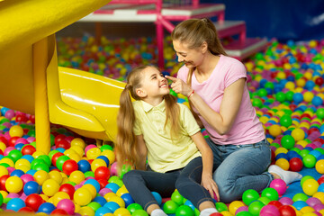 Obraz premium Loving mother and her child sitting in ball pit at indoor playground, copy space