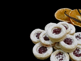 Strawberry Christmas biscuits and orange slices with cinnamon sticks on a black background