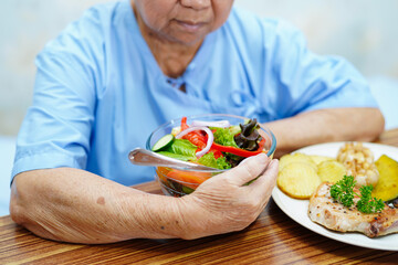 Asian senior or elderly old lady woman patient eating breakfast vegetable healthy food with hope and happy while sitting and hungry on bed in hospital.