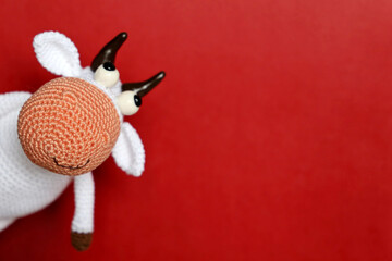 White knitted toy bull on red background, New Year greeting card with free copy space for text. Chinese Year of Bull, Zodiac symbol 2021