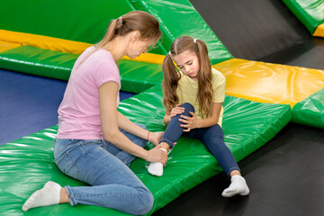 Trampoline jumping accident. Mom and child with foot injury sitting on rebounder at kids...