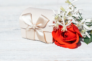 White satin gift box with a red rose on a white wooden background.Festive concept for Valentine's Day and Birthday.Selective focus.