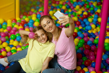 Fototapeta na wymiar Mother and daughter taking selfie together in ball pond at kids play center