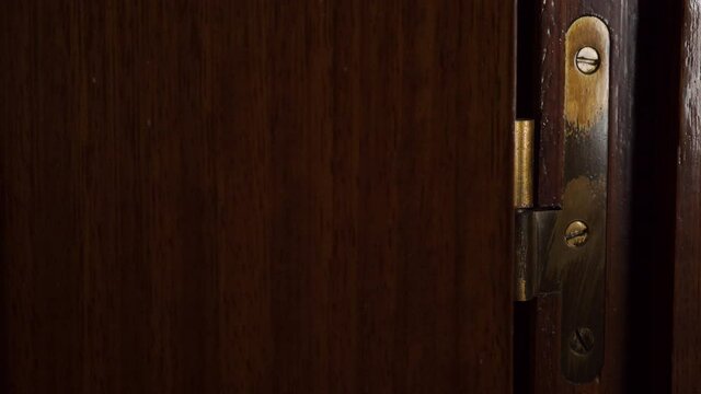 Closing scene of lacquered wood dark room door and golden old vintage hinge close up