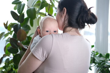 A beautiful young mother holds her newborn son in her arms by the window. Close-up portrait of a...