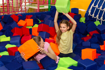 Lovely girl and her mom having lots of fun playing with soft cubes at indoor kids centre, copy space